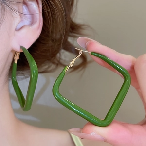 Detail of green square drop earrings with gold metallic clips worn by a model