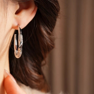 Close-up of a silver twisted C-shaped hoop earring with zircon inlay worn by a model