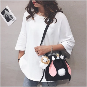 Detail view of black canvas bucket bag with pink bunny ears and white pom-pom tail