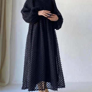 Detail of black lantern sleeve dress showing textured 3D polka dot fabric and flowy hemline