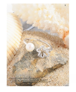 Detail of silver S925 flower ring with pearl on beach sand and white coral