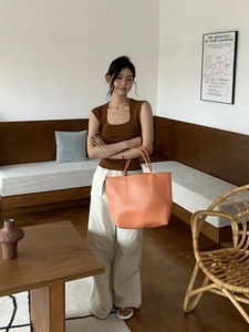 Detailed view of the vibrant orange woven straw tote bag with intricate texture and craftsmanship