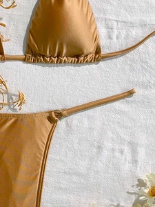 Flat lay of metallic bronze triangle bikini set with tie-side bottoms on white fabric
