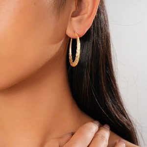 Close-up of golden geometric twisted hoop earrings with metallic texture on a female model