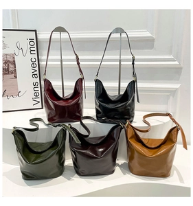 Multiple glossy patent leather Hobo bags in burgundy, green, and black on a white pedestal