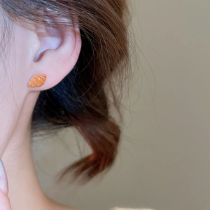 Dettaglio macro di un orecchino a lobo a forma di croissant con finitura arancione caramello