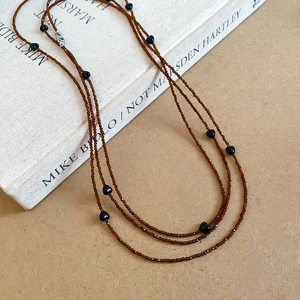Detail of layered brown crystal beaded necklace with black heart charms on paper background