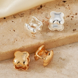 Elegant gold and silver four-leaf clover stud earrings displayed on natural stone