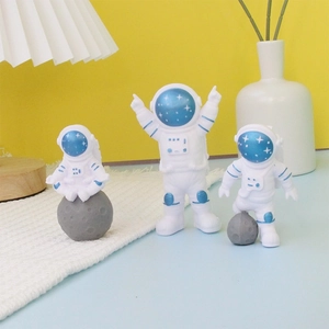 Three white astronaut cake toppers with blue details on grey planets for space theme party