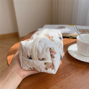 Close-up of quilted cotton makeup bag with bear pattern held against wooden table