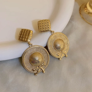 Detailed view of vintage gold woven straw hat earrings with bow on white ceramic tray