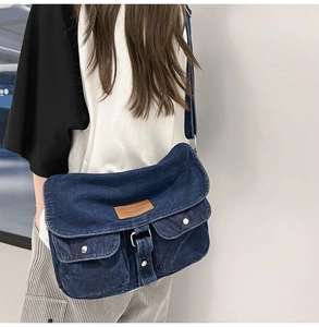 Détail du sac bandoulière en denim bleu avec deux poches avant et étiquette en cuir marron
