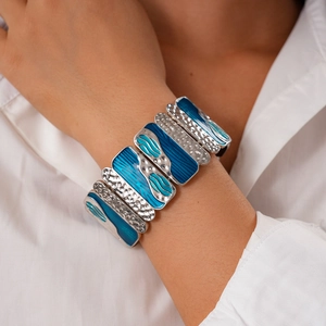 Close-up of a wide silver cuff bracelet featuring hammered metal and blue enamel waves