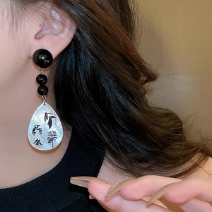 Close-up of mother-of-pearl drop earrings with black beads and ink-style bird painting