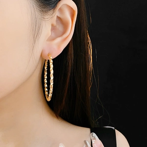 Close-up of textured golden hoop earrings featuring geometric faceted design on a model