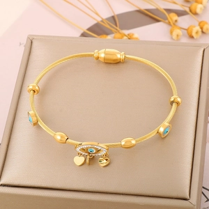 Close-up of golden steel cable bracelet with evil eye and heart charms on jewelry box