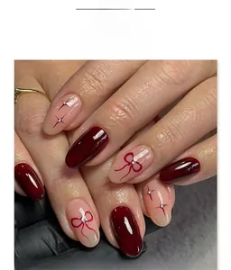 Detail of almond-shaped press-on nails with wine red bows and sparkling star accents