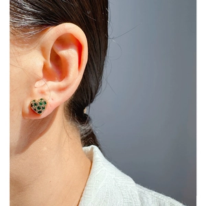 Elegant gold-plated heart earrings with green zircon stones worn on the ear model