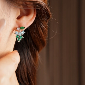 Detailed close-up of grape-shaped stud earring with green and white zircons on model ear