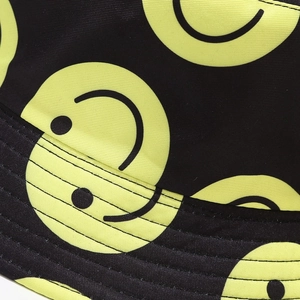Close-up of yellow smiley face print and parallel stitching on black bucket hat