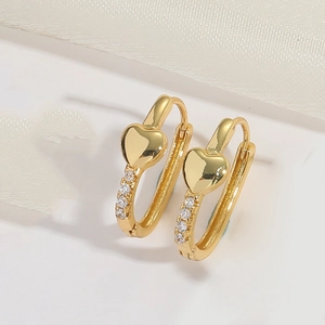Detail of gold heart huggie earrings with pave cubic zirconia on white silk background