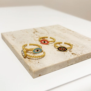 Detail of four colorful beaded evil eye rings on a neutral textured stone display