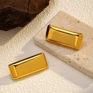 Close-up of polished gold rectangular geometric earrings on a textured stone display