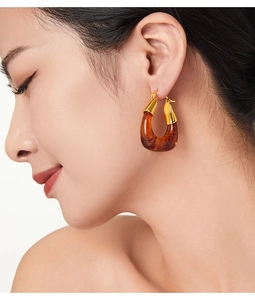 Close-up of vintage U-shaped resin earrings in amber and gold on model's ear