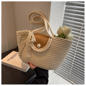 Detail of cream straw tote with brown leather flap, pearl buckle, and lace bow detail