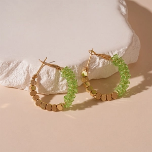 Détail de créoles avec perles dorées et pierres de cristal vert sur pierre