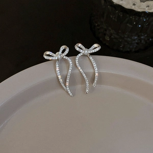 Close-up of silver bow stud earrings with sparkling cubic zirconia on a ceramic tray