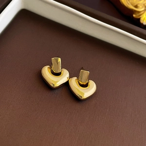 Detail of gold heart earrings with polished finish on dark brown background