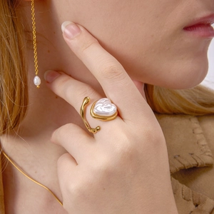 Anello in acciaio al titanio dorato con perla a forma di cuore sulla mano di una modella