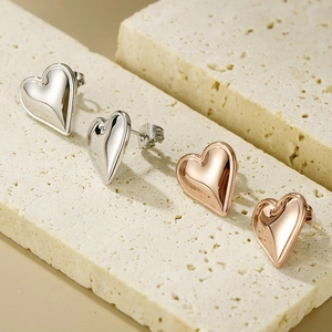 Macro shot of silver and rose gold heart earrings displayed on beige travertine stone