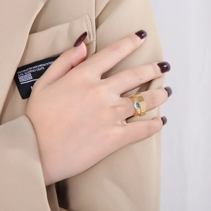Detail eines breiten goldenen Edelstahlrings mit blauem Auge-Stein an der Hand eines Modells