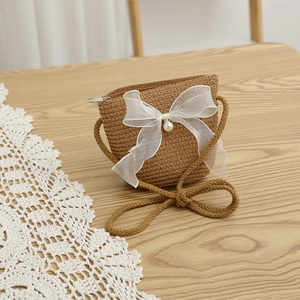 Detail of a khaki straw crossbody bag featuring a white organza bow and pearl accent