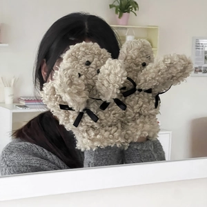 Détail de gants en peluche beige en forme de chiot avec nœud noir et texture douce