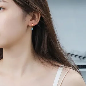 Elegant gold-plated hoop earrings featuring a brilliant blue zircon pendant on a model
