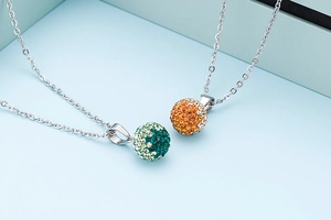 Detail of silver chain necklaces featuring sparkling green and orange rhinestone ball pendants