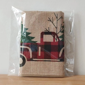 Detail of a Christmas flax garden flag with red plaid truck and green tree in polybag