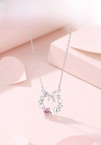 Detail of silver floral wreath necklace with bow, star, and pink zircon pendant