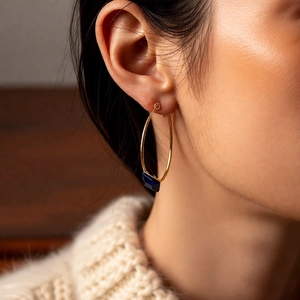 Close-up of 24k gold-plated hoop earring with a square blue gemstone on a model