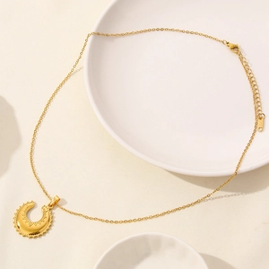 Close-up of golden crescent moon pendant with wavy texture on white porcelain plate