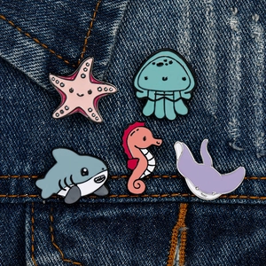 Set of five ocean animal enamel pins pinned on a blue denim jacket pocket