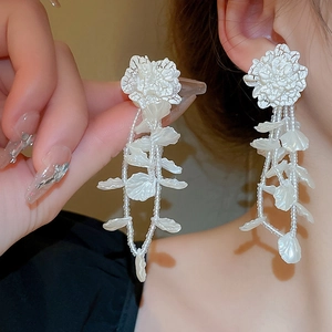 Detailed view of white floral tassel earrings with intricate beads on ear lobe