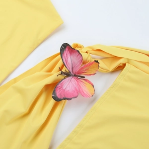 Détail de la robe jaune asymétrique avec accents papillon roses et design à nœuds