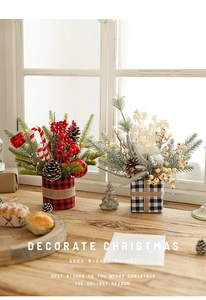 Close-up of Christmas pine branch pots with berries and plaid fabric on wooden surface