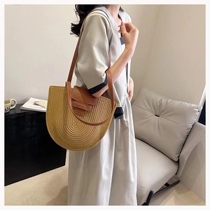 Model showcasing a half-moon beige woven cotton bag with brown leather strap and flap closure