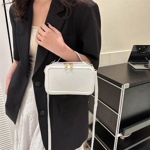 Minimalist white suitcase-style crossbody bag with gold zippers shown on a model