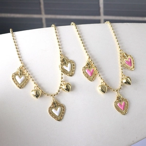 Close-up of golden beaded chain necklace featuring pink and white heart drip oil pendants
